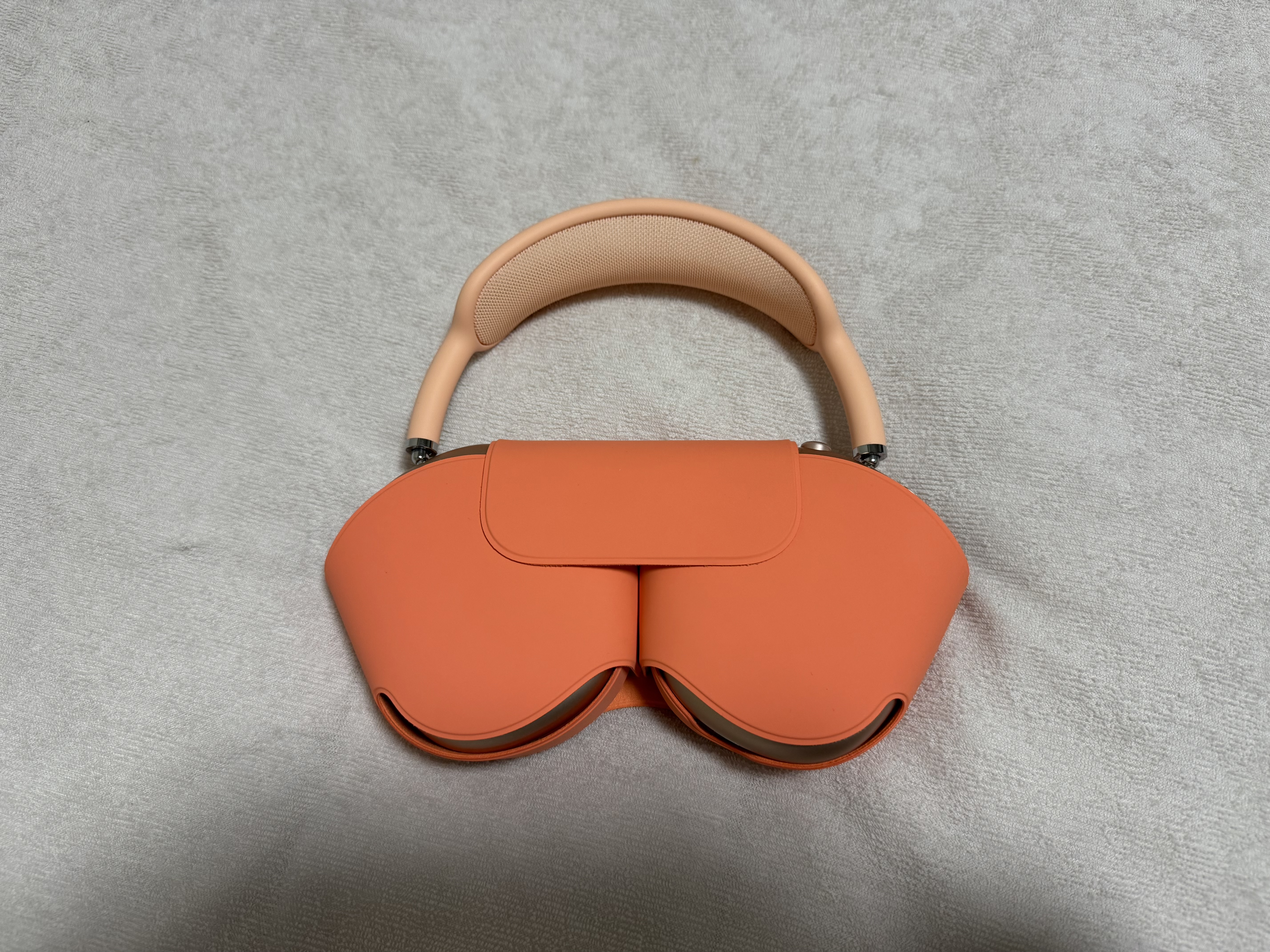 専用のスマートケースに収納された状態のAirPods Max本体の写真。高級感のあるケースと細身のヘッドバンドがまるでハンドバッグのようにも見えます。クリック/タップすると画像が切り替わります。