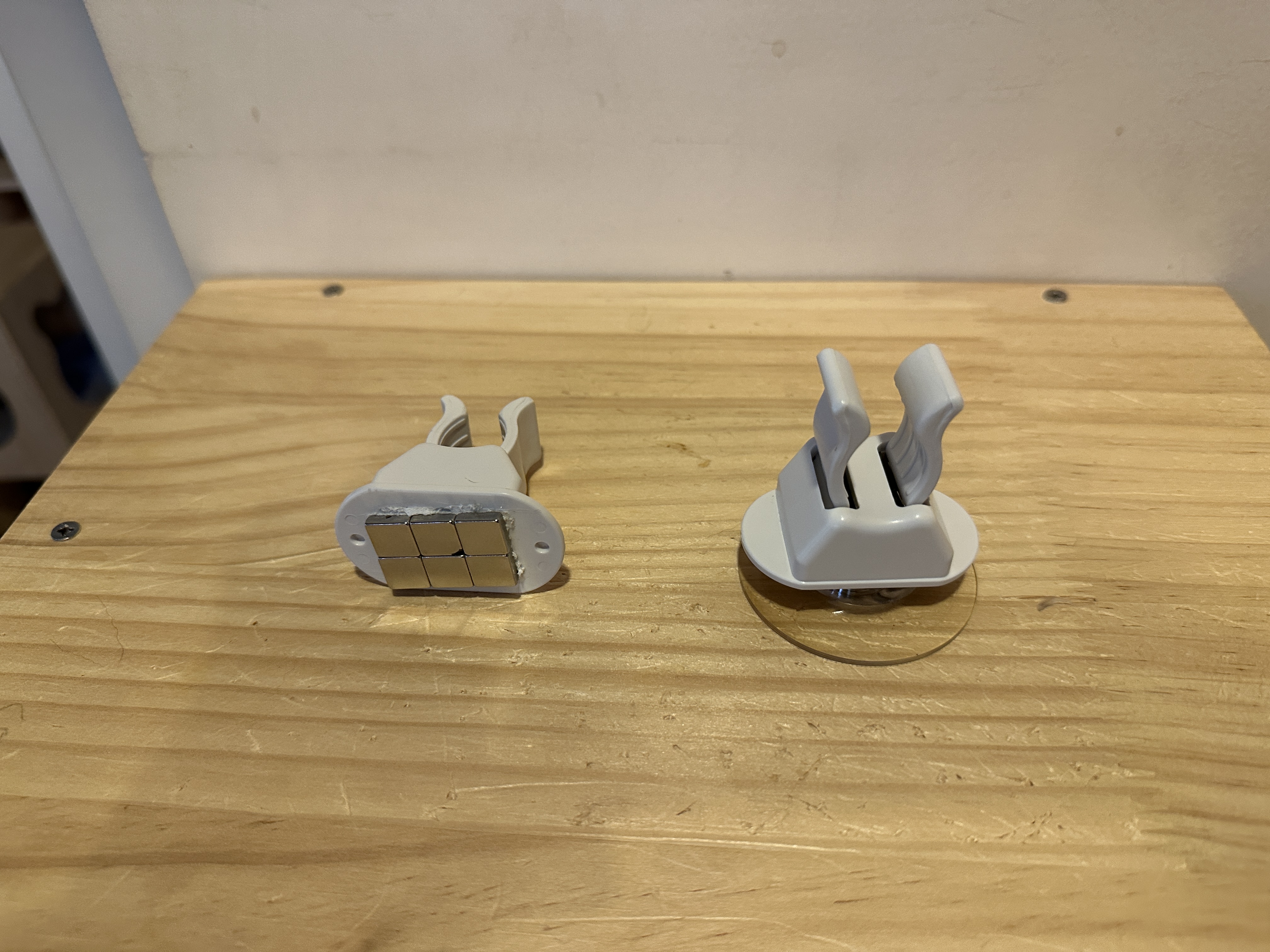 木製の台に置かれた、吸盤式・磁石式白杖ホルダーの写真。吸盤式は縦に、磁石式は底に張り付けられたマグネットが見えるように横向きに置いてあります。