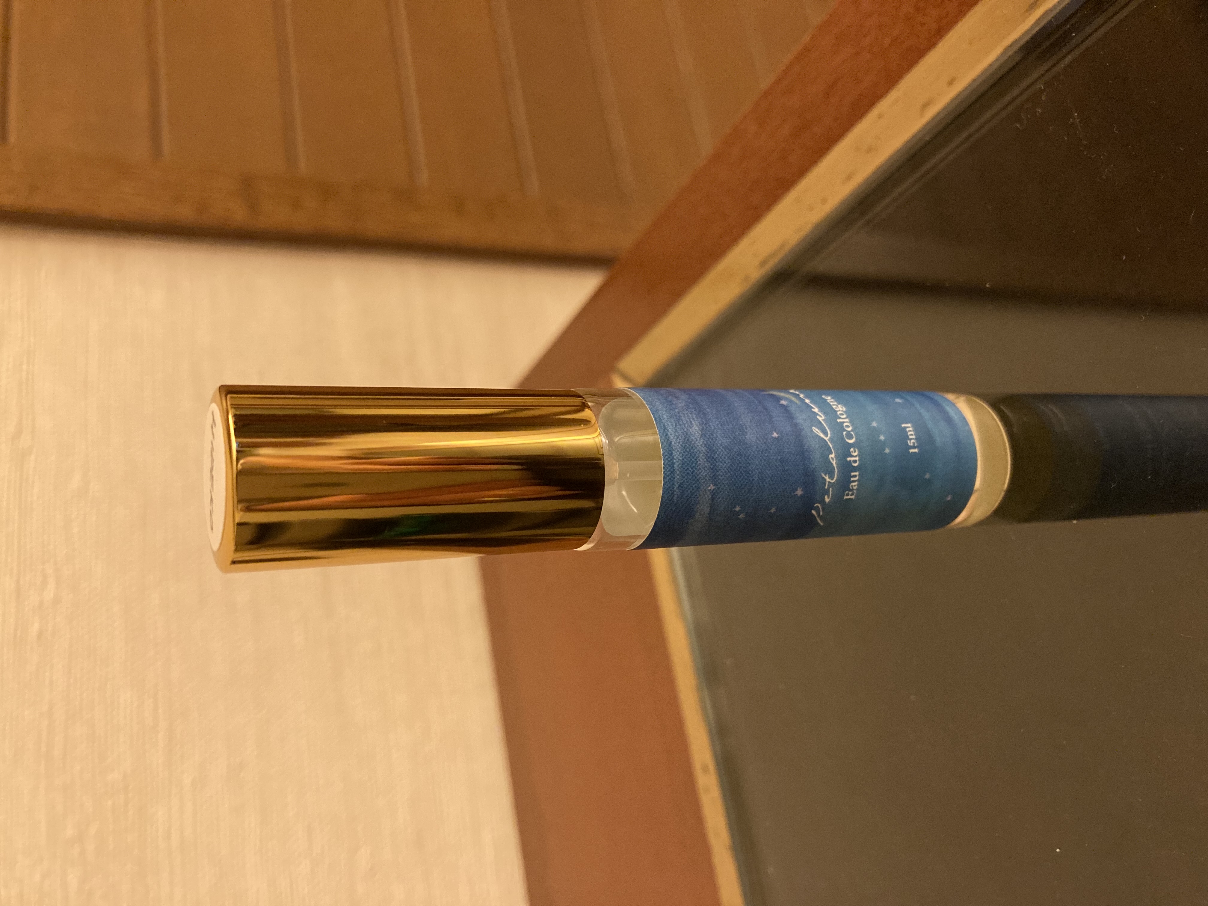 木製の台に置かれた手作り香水のボトル。キャップ部分は金色で、ボトルには星の描かれたターコイスブルーのラベルが貼られています。